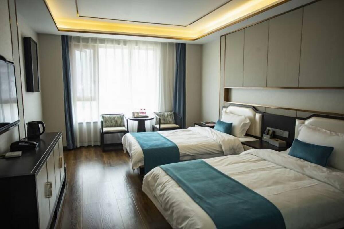 A hotel room with two beds, a desk, a chair, a TV, and a window with curtains.