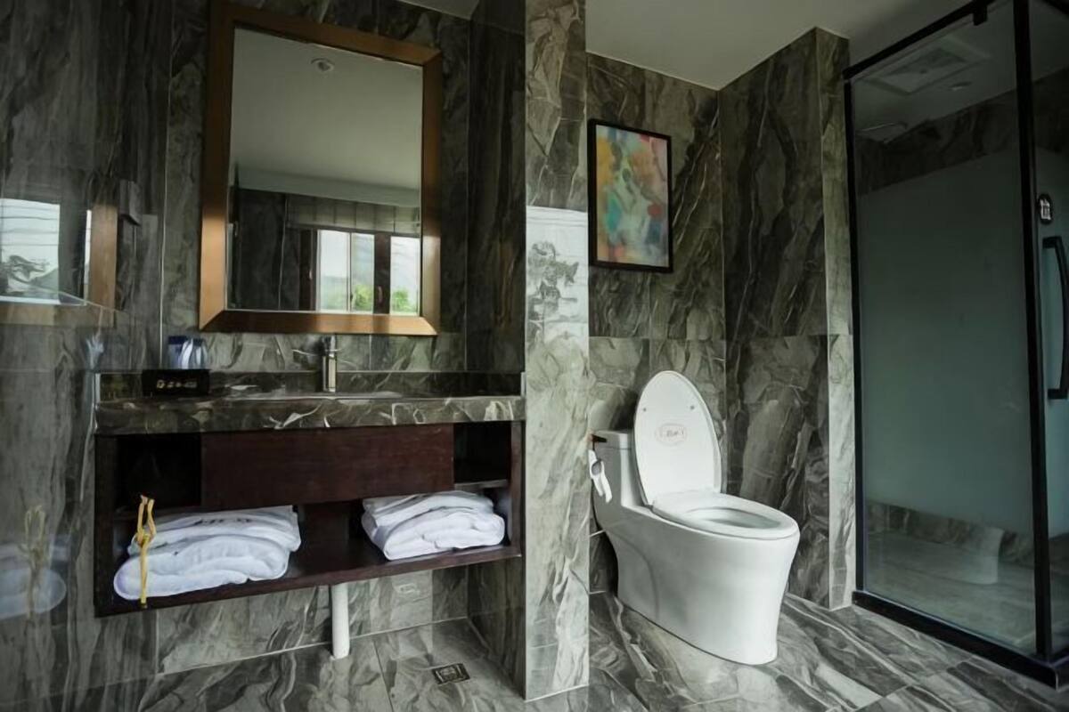 A bathroom with a marble wall, a white toilet, a sink with a mirror, and a towel rack.