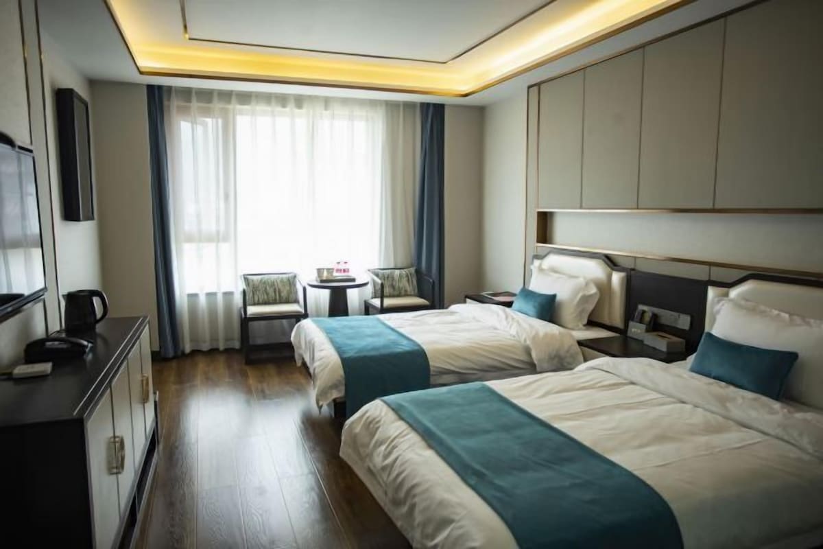 Habitación de hotel con dos camas, un escritorio, una silla y una ventana con cortinas.