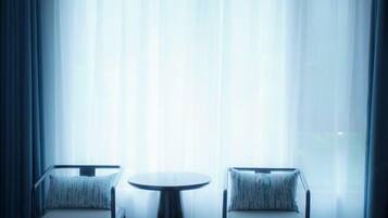 A room with two armchairs and a small round table, positioned in front of a large window with sheer curtains.