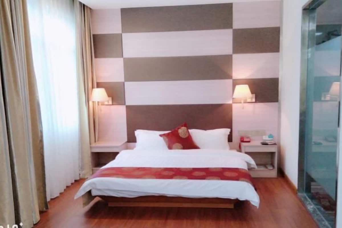 Een hotelkamer met een geruit patroon op de muur, een bed met witte lakens en een rode sierkussen, twee bedlampjes en een nachtkastje met een lamp.
