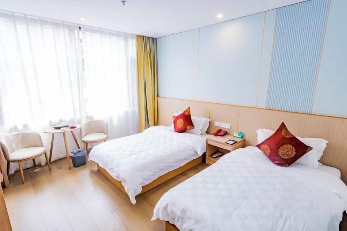 Een hotelkamer met twee bedden, een tafeltje, stoelen en een raam met gordijnen.