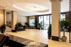 A spacious lobby with a central staircase, large windows, and potted plants.