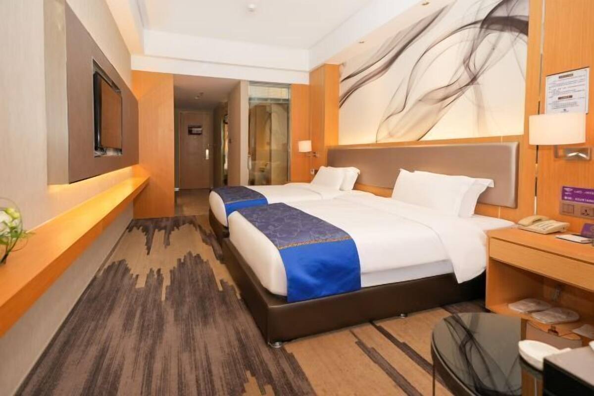 A hotel room with a large bed, a desk, a chair, a TV, and a painting on the wall.