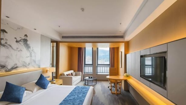 A hotel room with a bed, a desk, a chair, a TV, and a large window. - Ling Jiang Hotel (Yongtai)