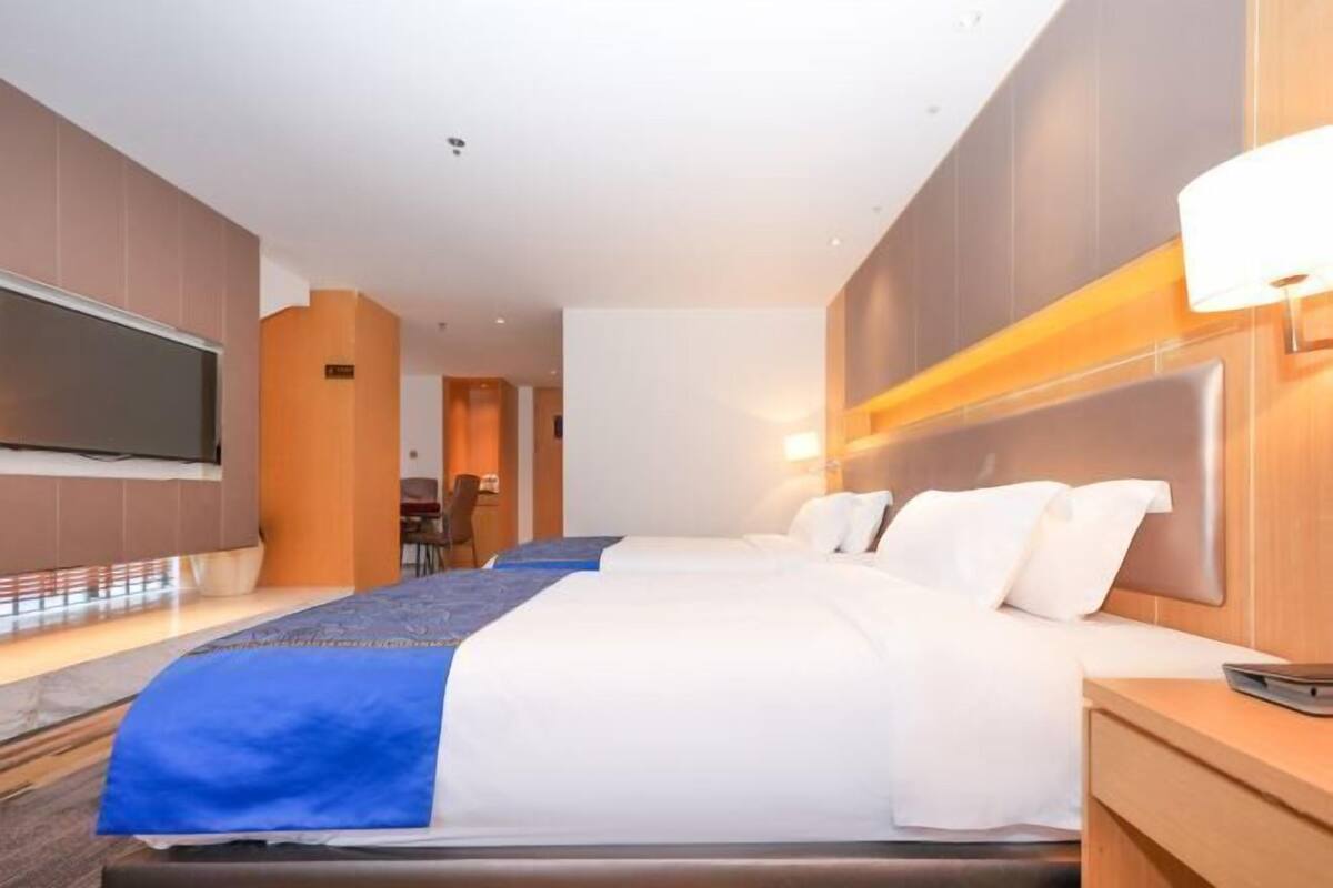 A hotel room with a large bed, a TV, and a desk with a lamp.