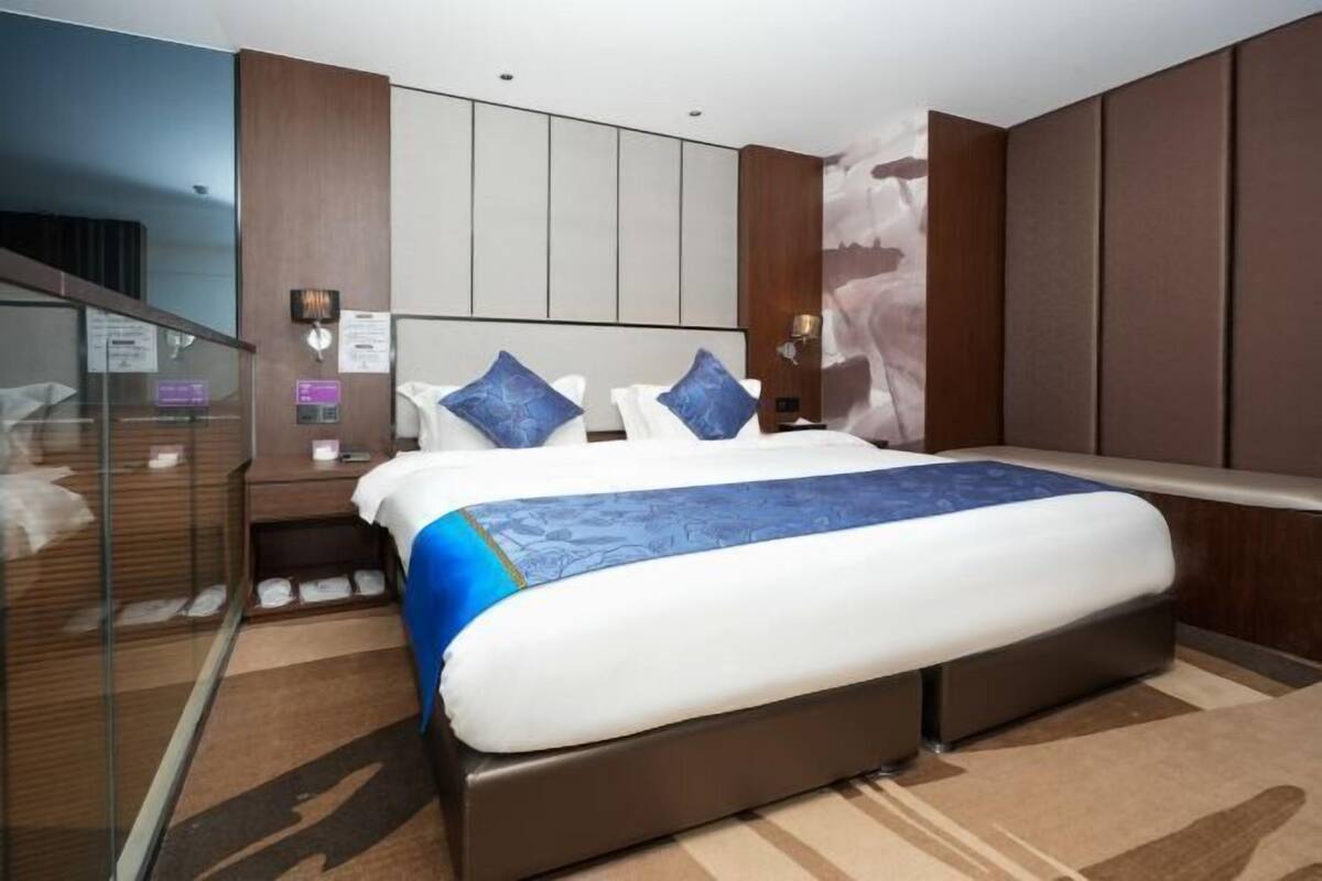 A modern hotel room with a large bed, a glass partition, and a wooden panel wall.