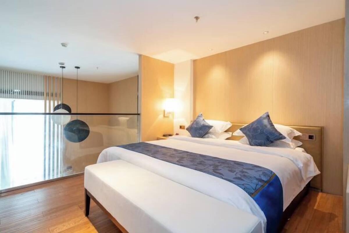 A modern hotel room with a large bed, bedside tables, a lamp, and a view through a glass door.