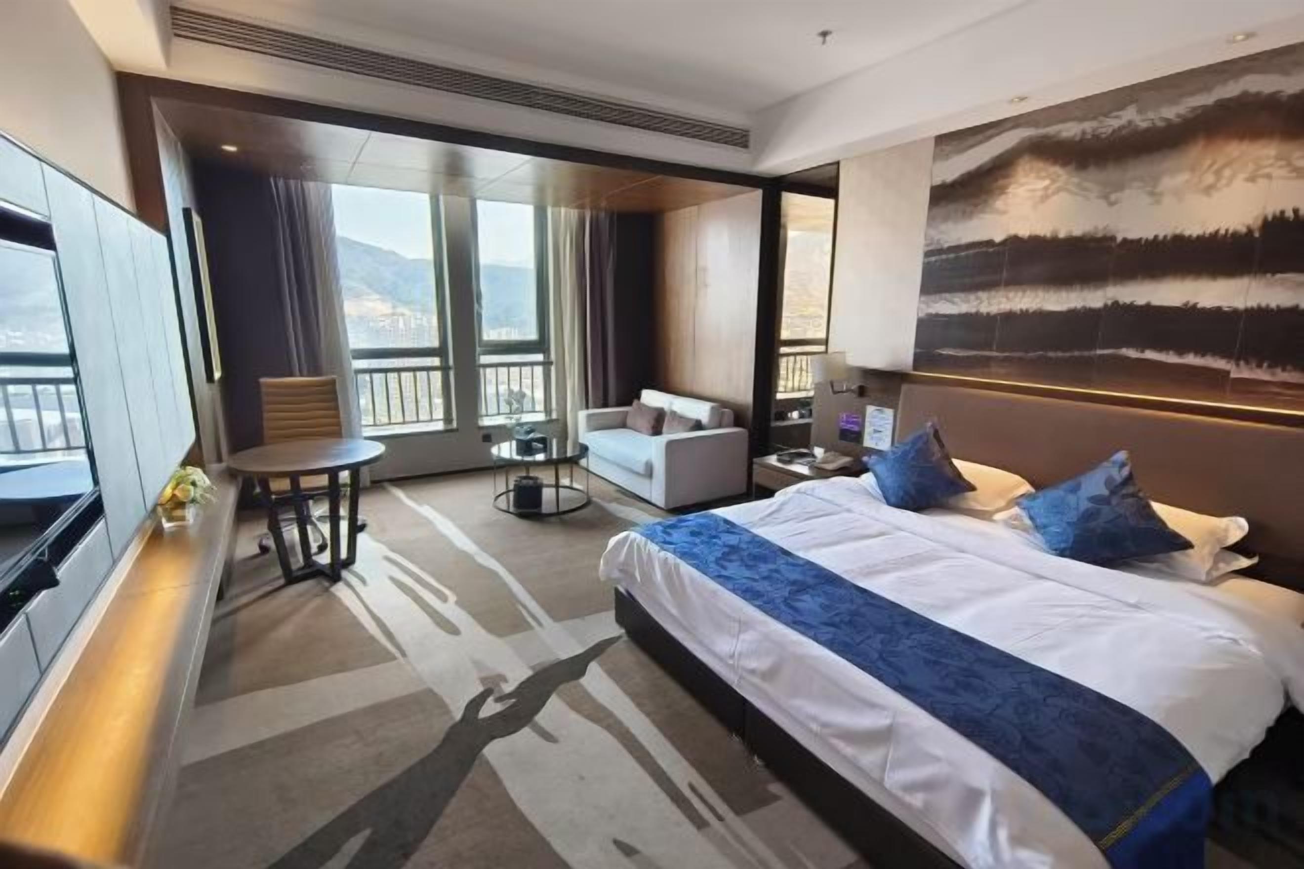 A hotel room with a large bed, a seating area with a table, and a view of the outdoors.