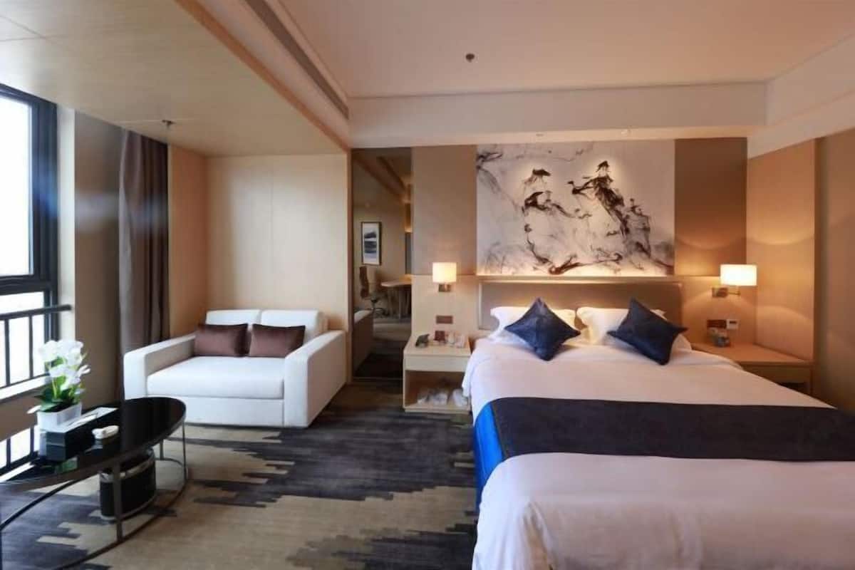 A hotel room with a bed, a sofa, a small table, and a wall-mounted artwork.