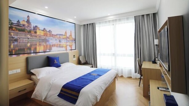 Een hotelkamer met een bed, een bureau, een televisie en een groot raam met gordijnen.