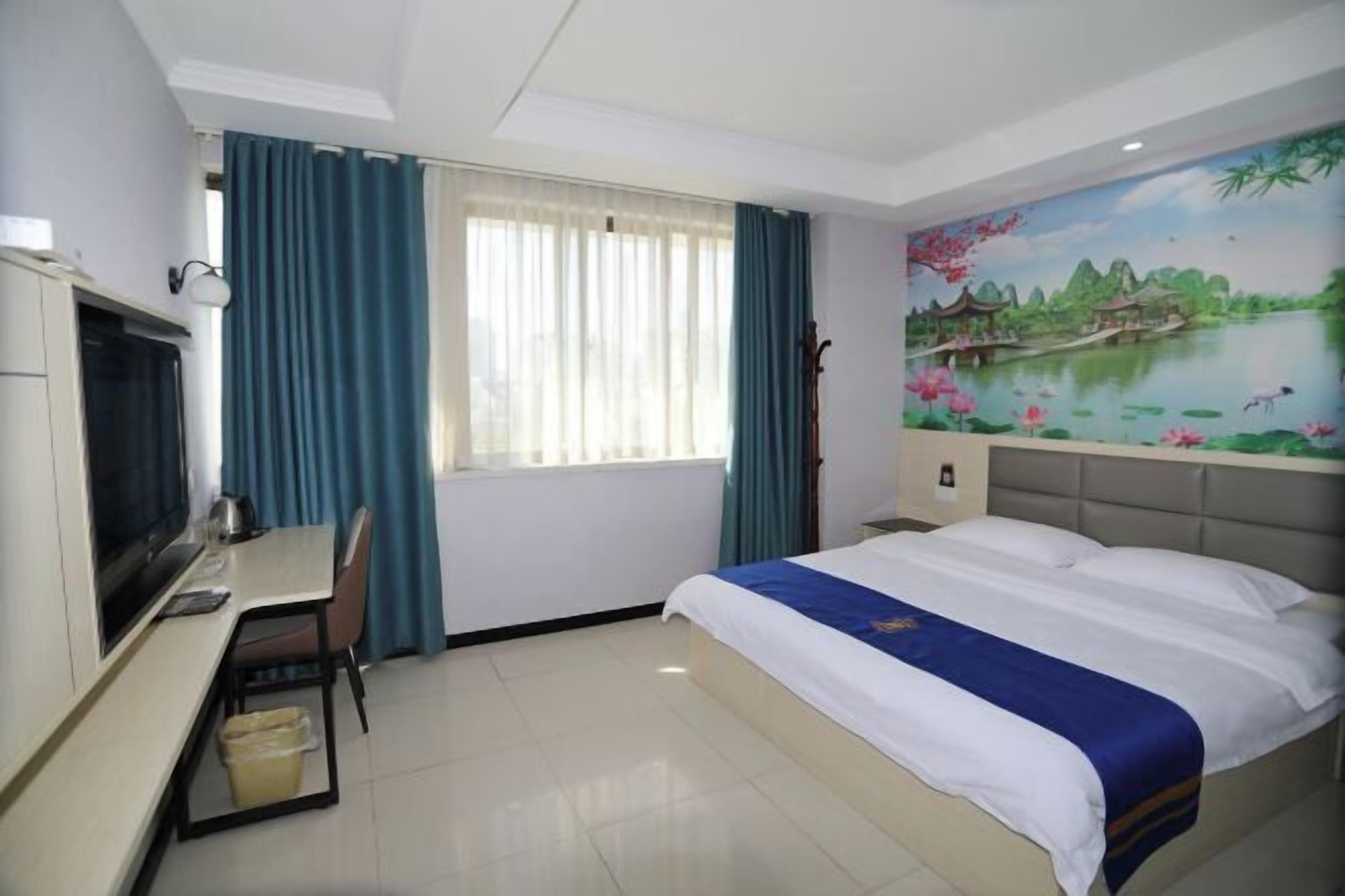 A hotel room with a bed, a desk with a chair, a television, and a window with curtains.