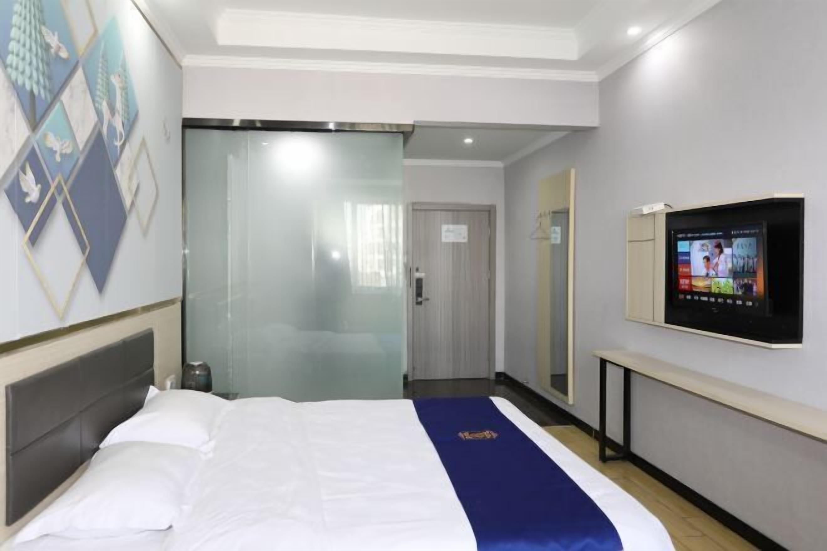 A hotel room with a bed, a television, and a glass door leading to a bathroom.