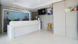 Een hotel receptie met een wit receptiebalie, een aan de muur bevestigde televisie en een poster.