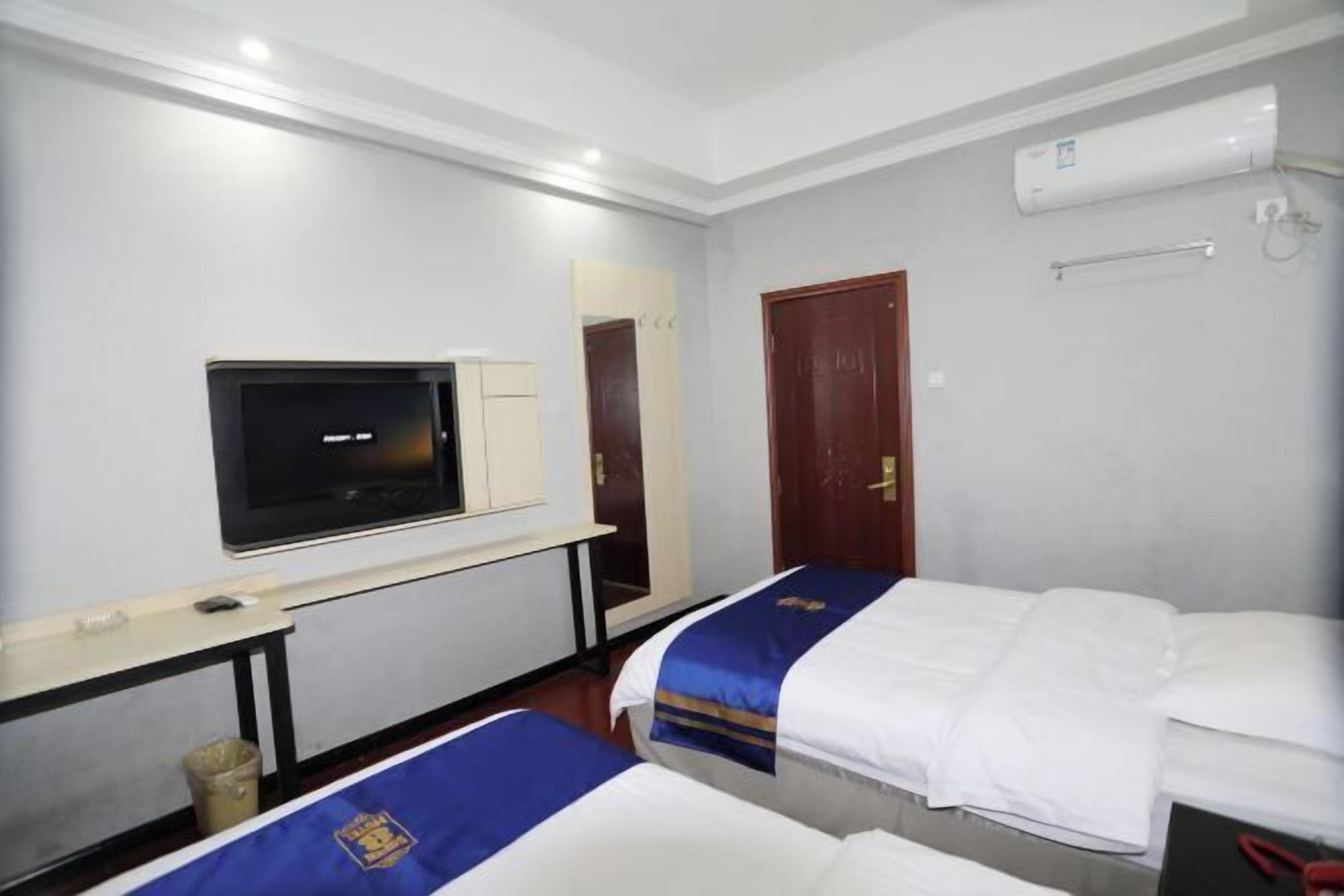A hotel room with two beds, a TV, a desk, a mirror, and an air conditioning unit.