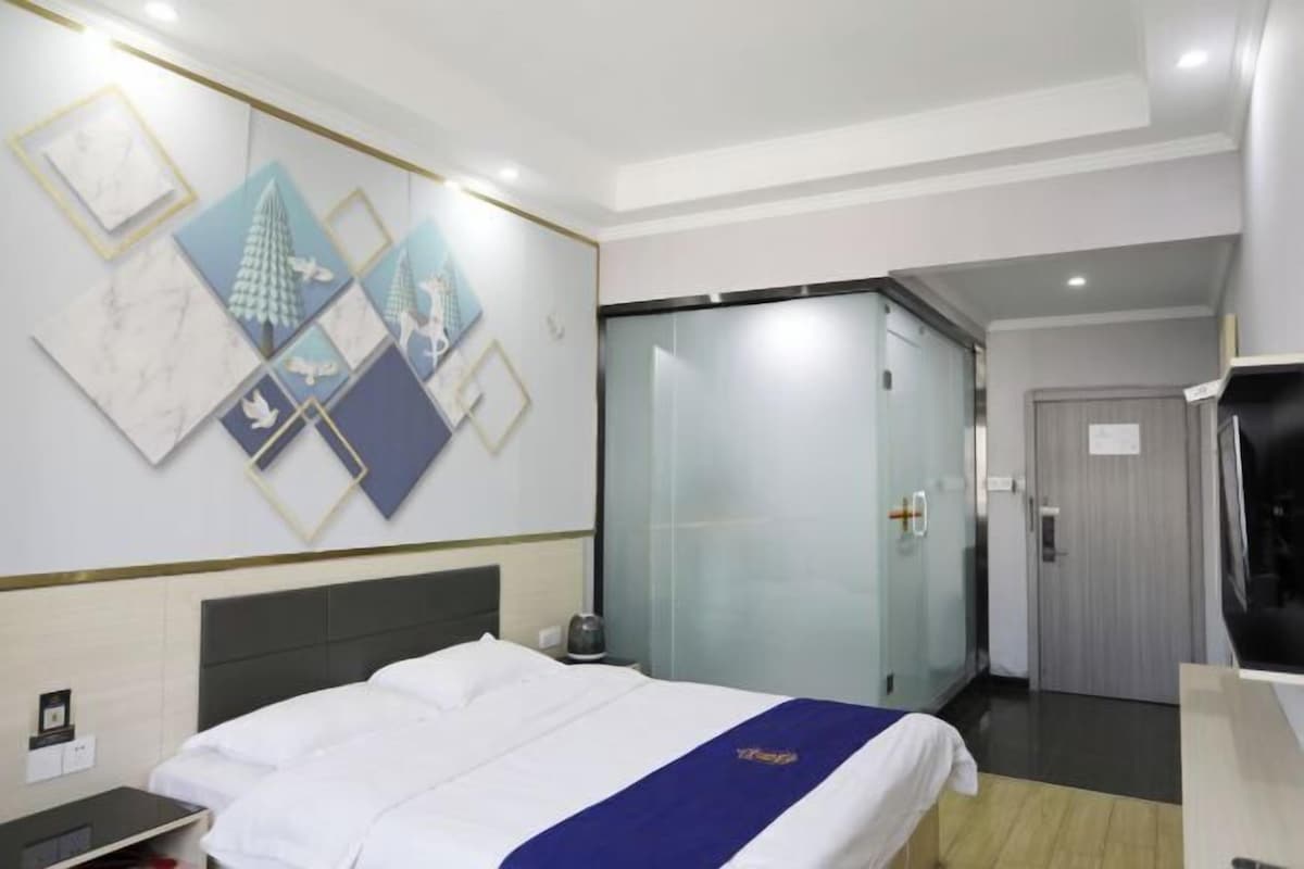 A hotel room with a bed, a nightstand, a glass door closet, and artwork on the wall.