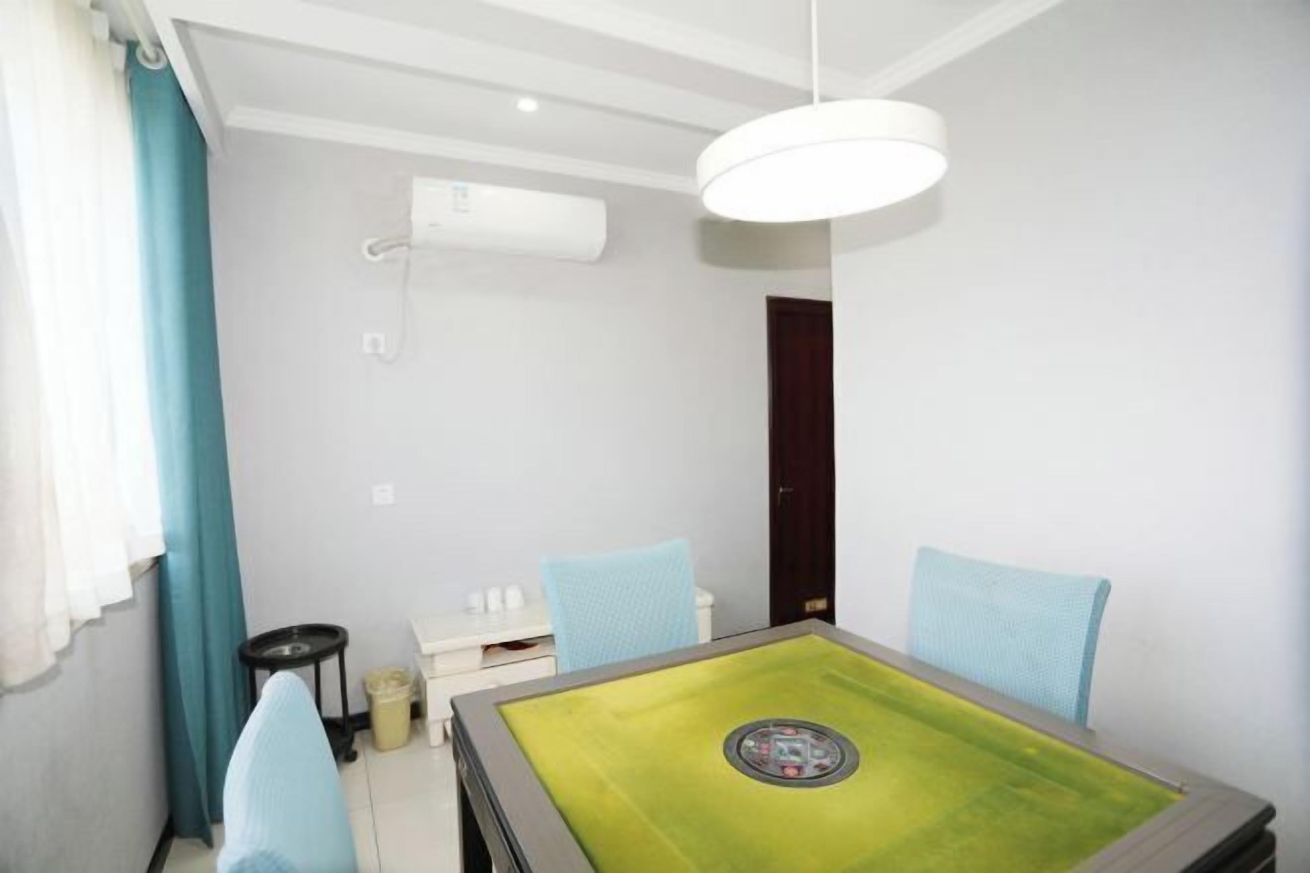 A room with a green table, two blue chairs, a white ceiling light, and a white air conditioning unit.