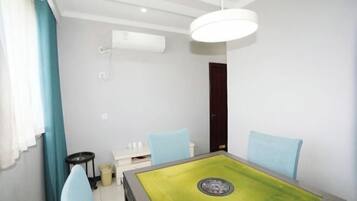 A room with a green table, two blue chairs, a white ceiling light, and a white air conditioning unit.