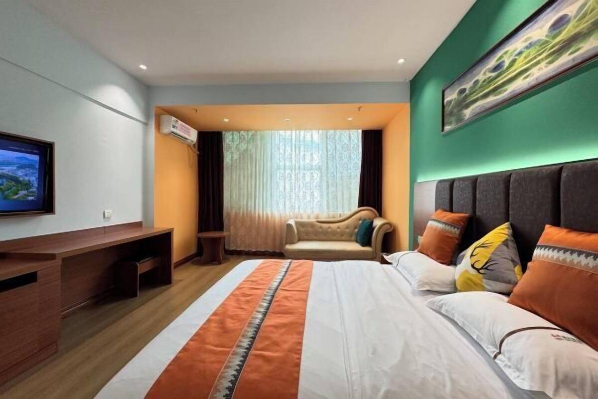 Een hotelkamer met een bed, een televisie, een bank en een raam met gordijnen.