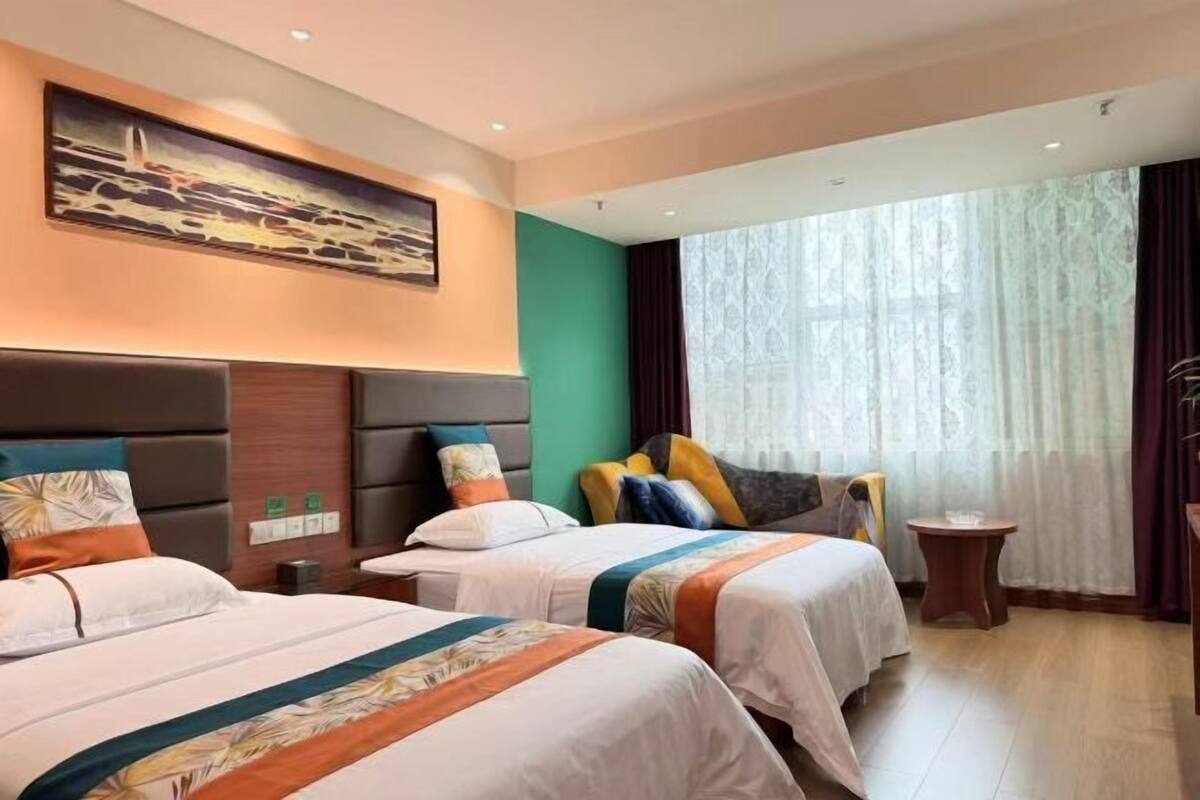 Een hotelkamer met twee bedden, een schilderij aan de muur, een raam met gordijnen en een kleine tafel.