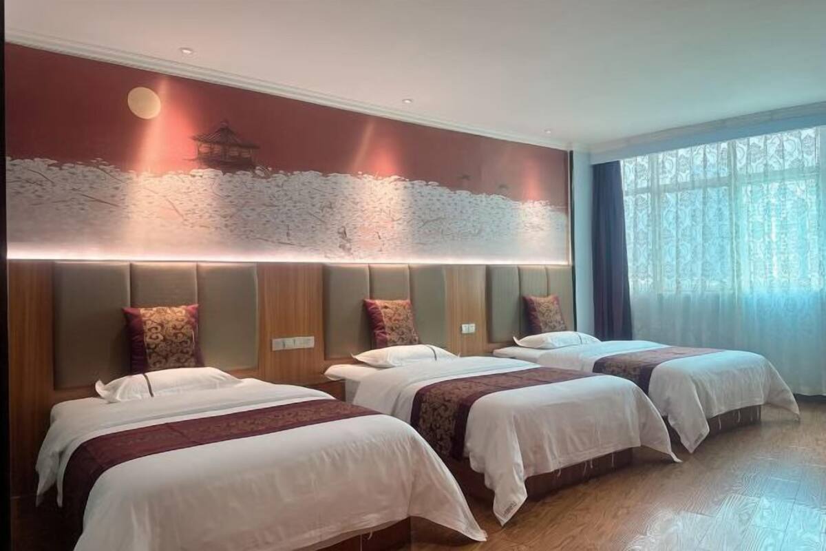 Een hotelkamer met drie bedden, een muurschildering en een groot raam met gordijnen.