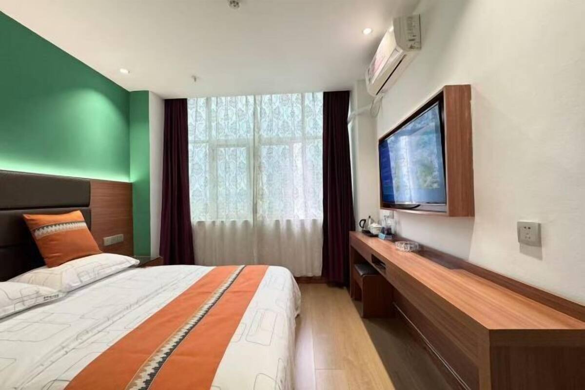 Een hotelkamer met een bed, een aan de muur bevestigde televisie, een bureau en een raam met gordijnen.