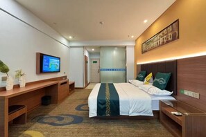 Une chambre d’hôtel avec un lit, une table de chevet, une télévision, un bureau et une petite plante.
