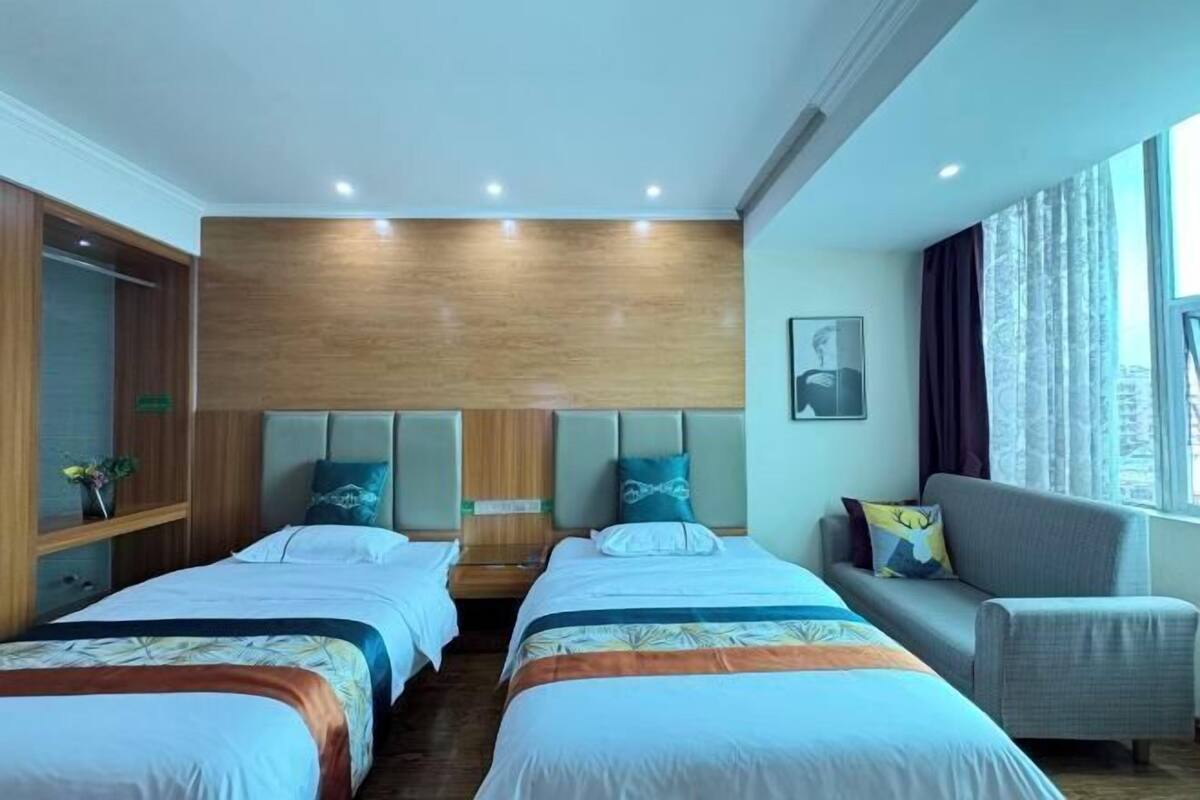 Een hotelkamer met twee bedden, een bank, een houten hoofdbord en een groot raam.