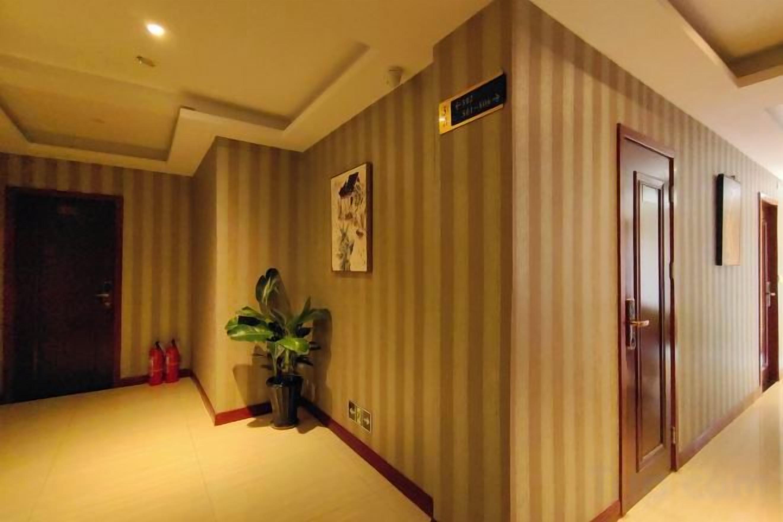 Un pasillo de hotel con paredes a rayas, una planta en maceta y un extintor.