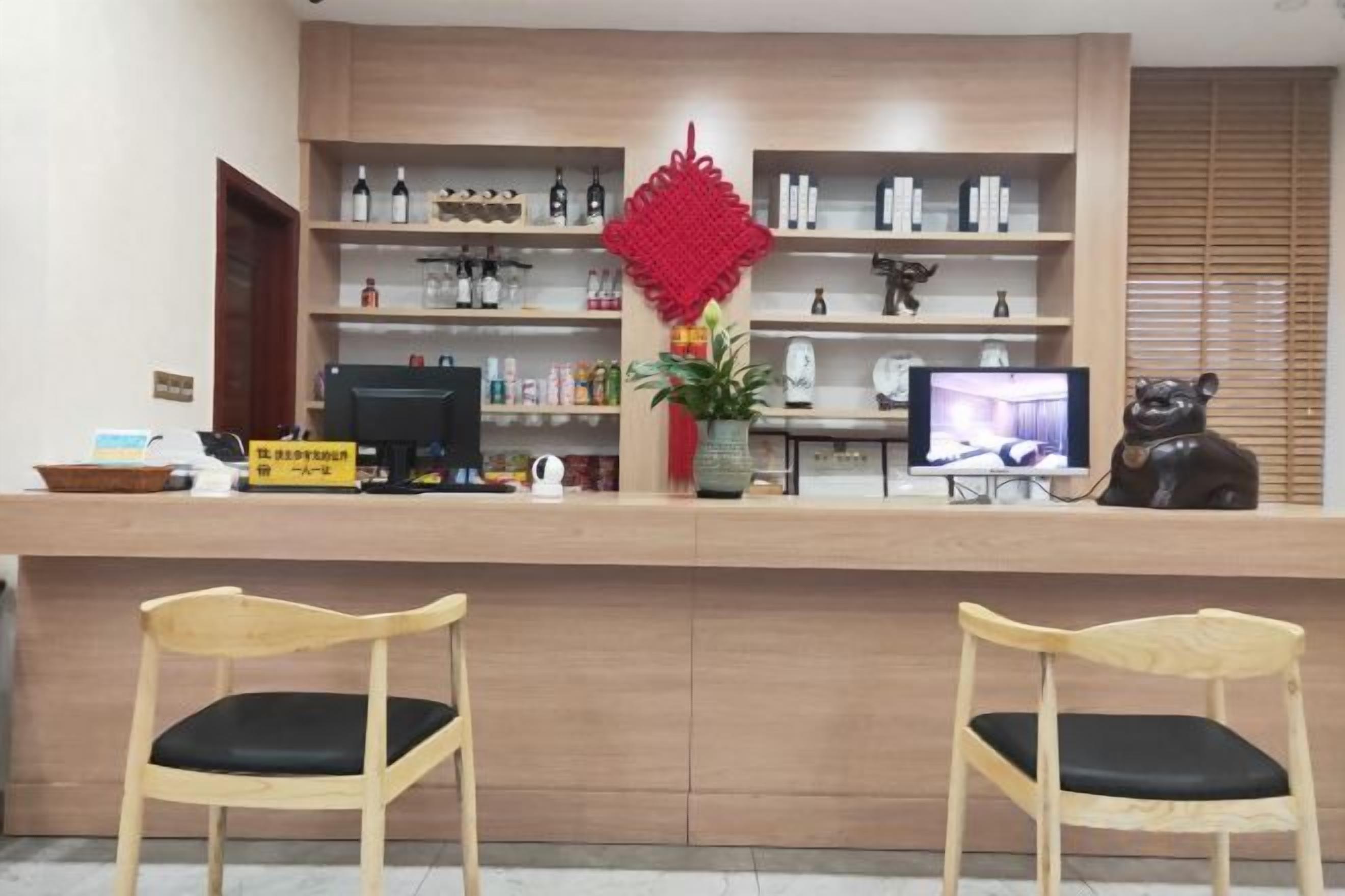 Un mostrador de recepción con una computadora, un televisor y un adorno rojo. Hay dos sillas de madera frente al mostrador.