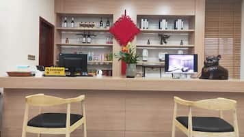 Un mostrador de recepción con una computadora, un televisor y un adorno rojo. Hay dos sillas de madera frente al mostrador.