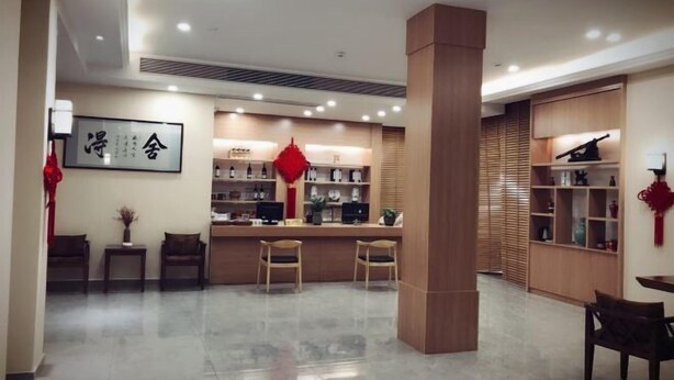 Een moderne hotellobby met een receptiebalie, een zithoek en houten schapverlichting met decoratieve objecten.