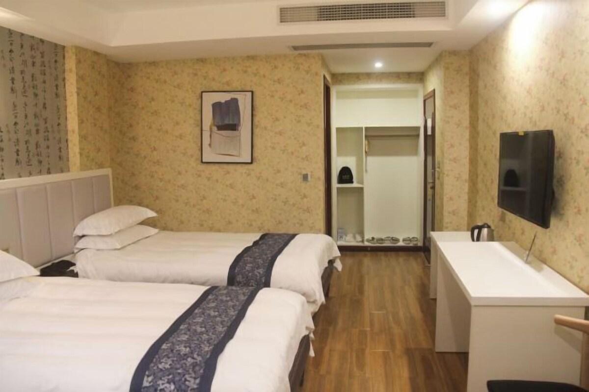 A hotel room with two beds, a desk, a mirror, and a TV.