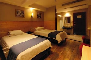 Une chambre d’hôtel avec deux lits, un plancher en bois, une table de chevet, un bureau, une chaise, un miroir et un tableau au mur.