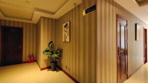 Een hotelgang met gestreepte behang, een potplant en een deur met een bordje.