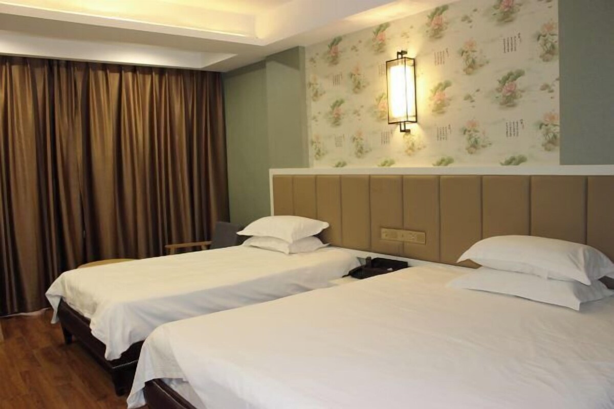 A hotel room with two beds, a desk, a chair, and a floral wallpaper.