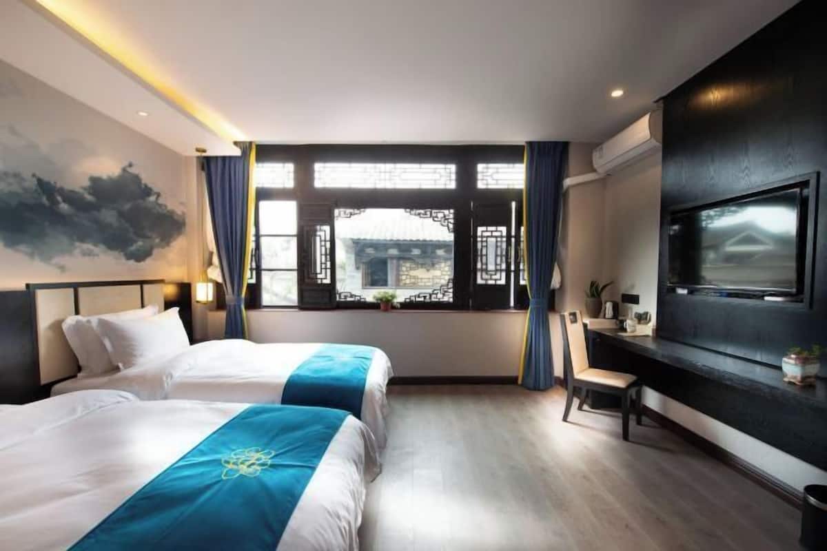 Habitación de hotel con dos camas, un ventanal grande con detalles arquitectónicos chinos tradicionales, un televisor de pantalla plana montado en la pared y una pequeña mesa con una silla.