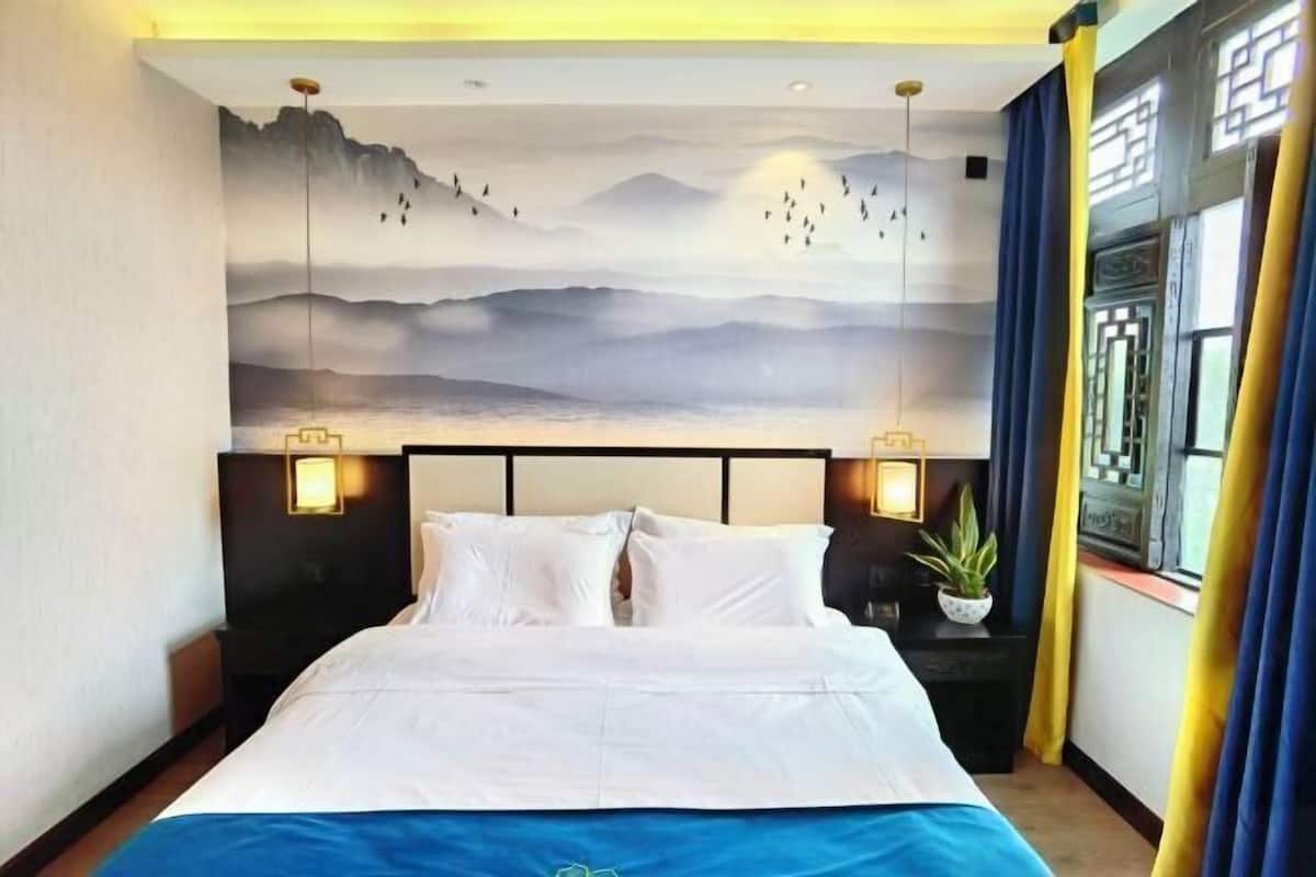 Una habitación de hotel con una cama grande, un mural en la pared y una ventana con cortinas.