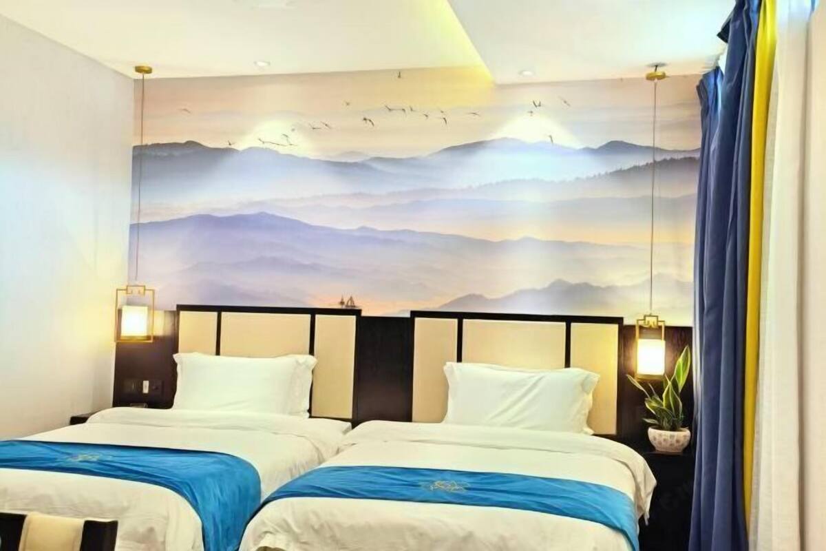 Habitación de hotel con dos camas, un mural de montañas y una planta en maceta.