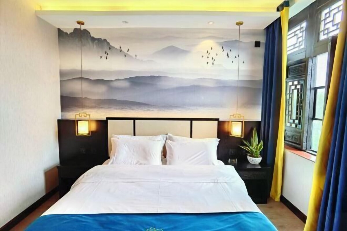 A hotel room with a large bed, a wall mural, and a window with curtains.