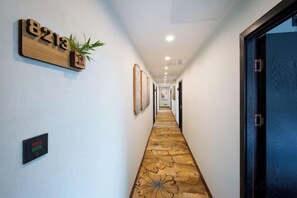 A hotel hallway with a carpeted floor, framed pictures on the walls, and a door on the right. - Qinqi Inn (Kunming)