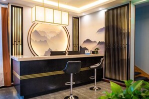 A reception area with a counter, two bar stools, a decorative wall with a mountain design, and a sliding door. - Qinqi Inn (Kunming)