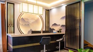 A reception area with a black counter, two bar stools, a decorative wall with a mountain design, and a hanging light fixture. - Qinqi Inn (Kunming)