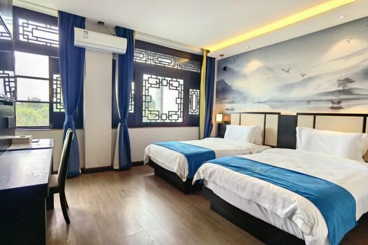 A hotel room with two beds, a desk, and a window with curtains.
