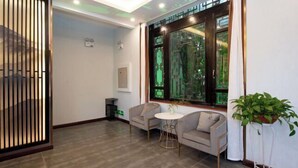 A modern room with a sofa, two chairs, a small round table, a large window with a view, and a potted plant. - Qinqi Inn (Kunming)