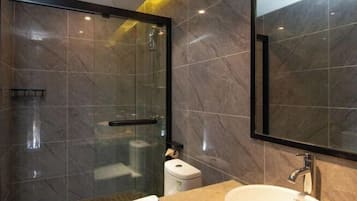 A modern bathroom with a glass-enclosed shower, a white sink, and a marble-tiled wall.