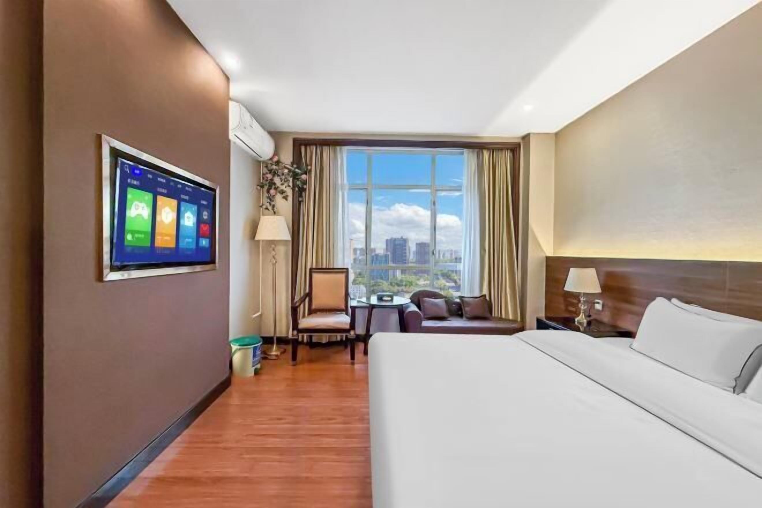 A hotel room with a large bed, a desk, a chair, and a TV mounted on the wall.
