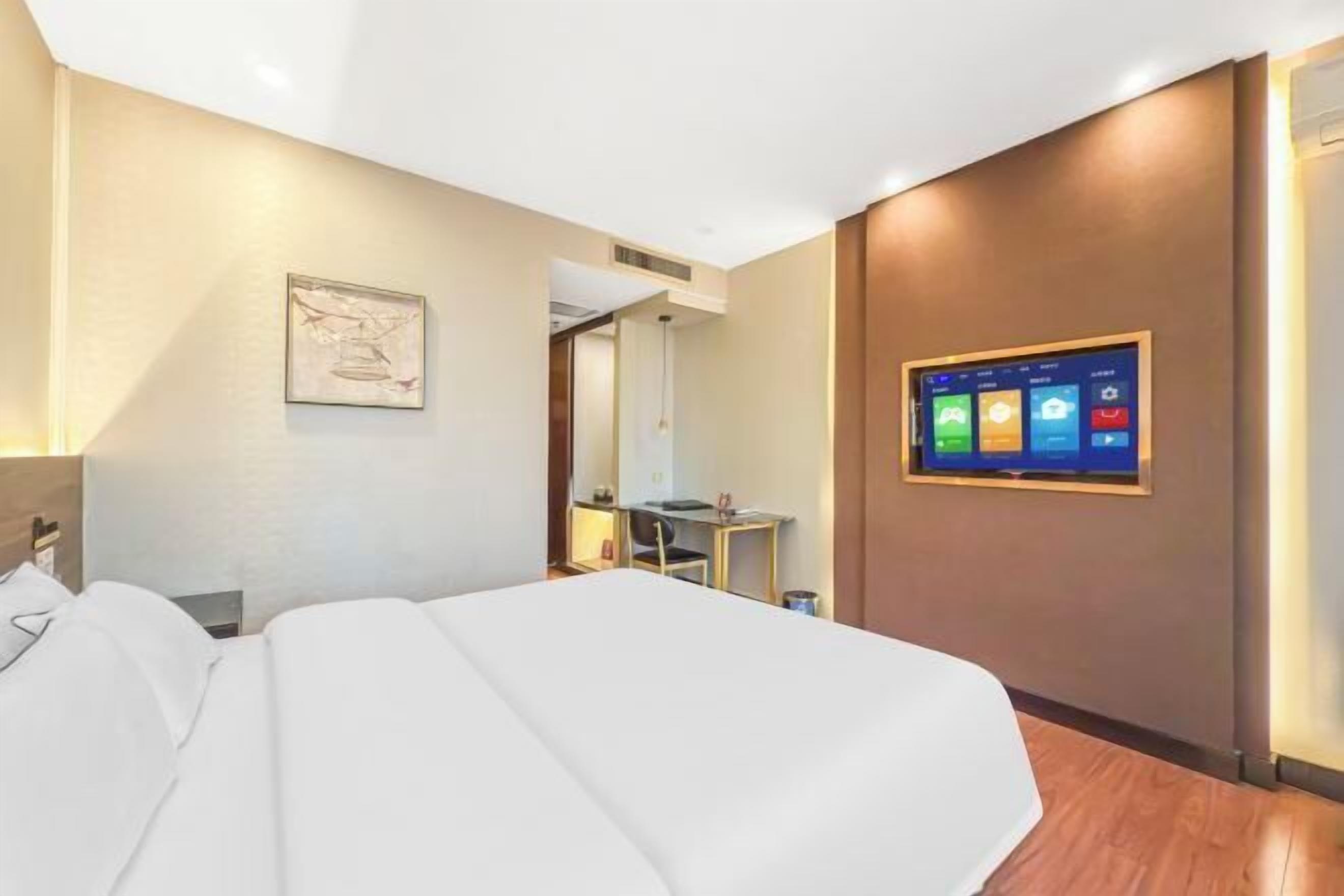 A hotel room with a bed, a desk, a chair, and a wall-mounted TV displaying a hotel app.