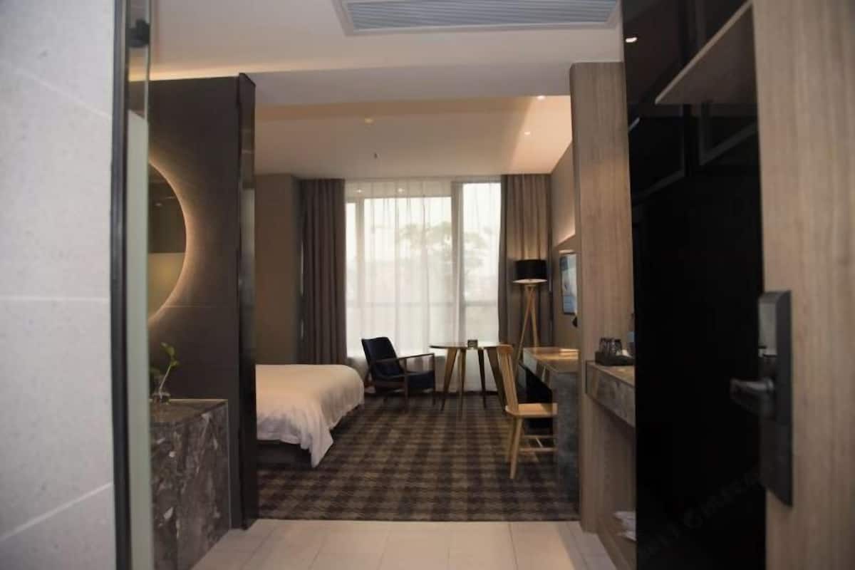A hotel room with a bed, a desk, a chair, a TV, and a large window.