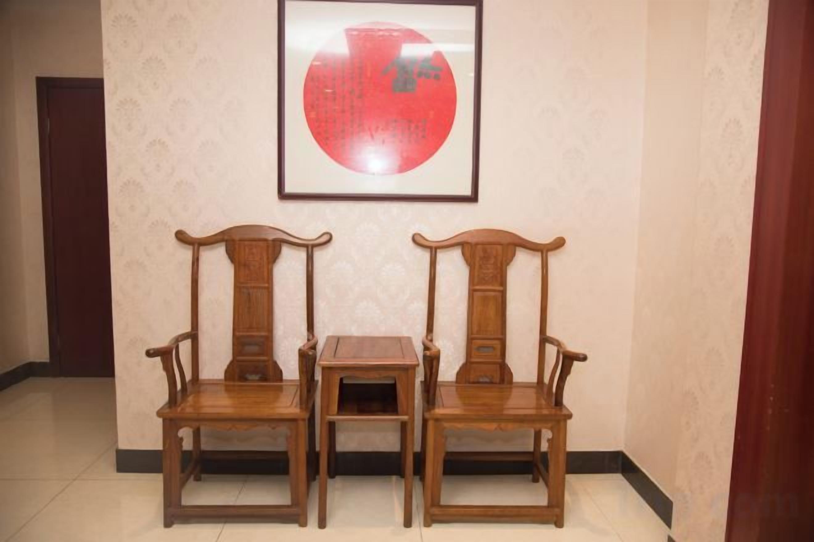 Een kamer met twee houten stoelen en een klein tafeltje, een kunstwerk in een lijst aan de muur, en behang met een patroon.
